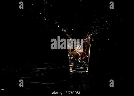 Movimento di spruzzi d'acqua ad alta risoluzione da un bicchiere d'acqua pulito mantenuto su un vassoio di raccolta in legno, isolato su sfondo nero Foto Stock