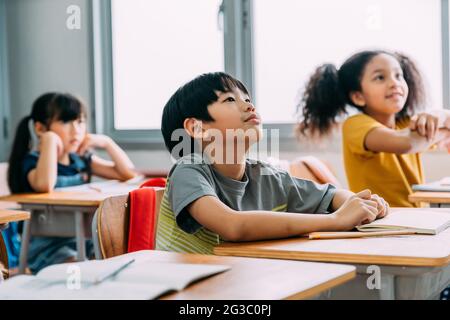 Curiosi ed eccitati piccoli ragazzi e ragazze carini che ascoltano e frequentano la lezione mentre si concentrano e si concentrano sugli studi in classe Foto Stock