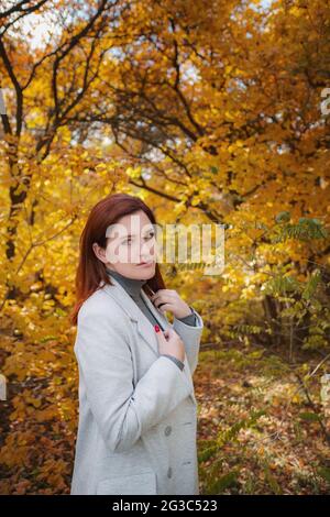 Una bella donna con testa rossa in buoni spiriti posa in un giorno d'autunno, godendo il bel tempo. Il concetto e l'idea di godersi la vacanza autunnale e autunnale Foto Stock