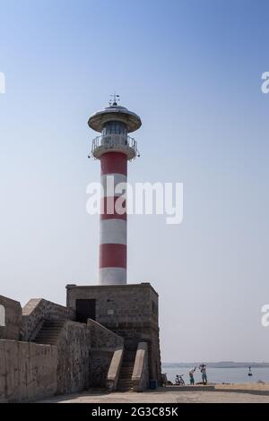 Una vista del porto con un grande vecchio faro rosso bianco, molo contro il cielo blu e il mare Foto Stock