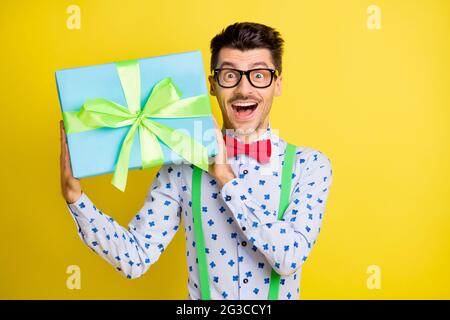 Ritratto di attraente ragazzo allegro che indossa una camicia di stampa che tiene in mani giftbox isolato su sfondo giallo brillante Foto Stock