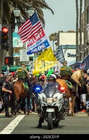 I sostenitori caucasici di Donald Trump marciano per protestare contro la sconfitta elettorale del 2020 a Huntington Beach, California, mentre un poliziotto motociclistico li mantiene confinati Foto Stock