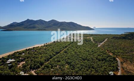 Vista aerea su un insediamento di fronte alla spiaggia di Bushland con un lungo tratto di spiaggia di sabbia e sfondo di un'isola di montagna Foto Stock