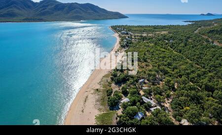 Vista aerea su un insediamento di fronte alla spiaggia di Bushland con un lungo tratto di spiaggia di sabbia e sfondo di un'isola di montagna Foto Stock