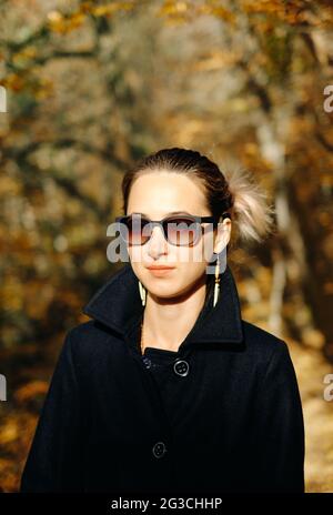 Ritratto di una donna che è elegantemente vestita con un cappotto nero e occhiali da sole. Foto Stock