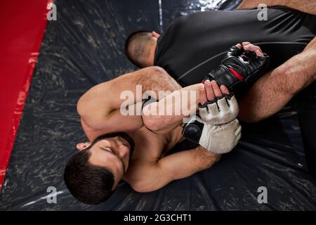 Grappler cercando di soffocare l'avversario in lotta a terra, allenamento in palestra. Due uomini atletici impegnati in mma, pugilato, lotta senza regole. Vista dall'alto Foto Stock