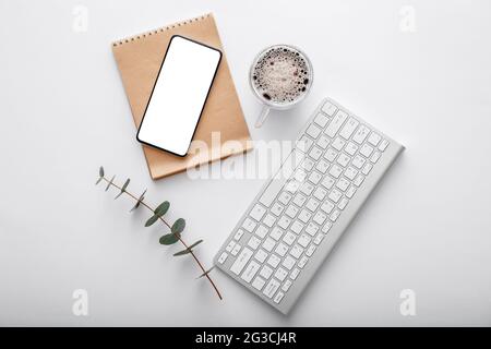 Smartphone mock-up con tastiera nota caffè tazza verde pianta su scrivania spazio di lavoro bianco. Vista dall'alto in piano. Telefono cellulare su un moderno spazio di lavoro Foto Stock