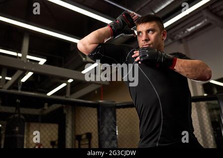 Indossa un pugile da uomo forte in guanti in piedi in posizione di combattimento durante l'allenamento. Concetto di strentgh e motivazione. Kickboxing, mma, concetto sportivo Foto Stock