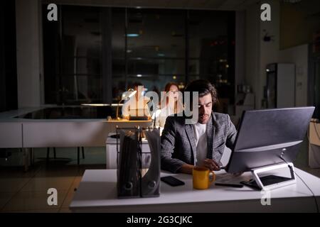 Team di dirigenti impiegati che lavorano al progetto molto tardi, utilizzando il computer. Persone che lavorano sodo in abbigliamento formale impegnate nel lavoro, nel pensiero, nel brainstormi Foto Stock