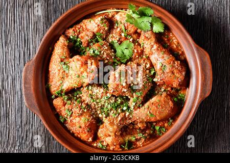 Chakhokhbili, pollo stufato, pomodoro con erbe fresche, noci e spezie in una pentola di argilla su un tavolo di legno con ingredienti su un tagliere, georgia Foto Stock