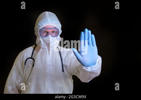 Un medico in un vestito protettivo covid fa un gesto di arresto con la sua mano Foto Stock