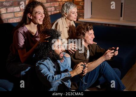 le persone che si divertono a giocare in un videogioco, riposarsi a casa. gli amici si divertono durante il gioco , entusiasti millennial diversi amici americani divertirsi con gioia Foto Stock