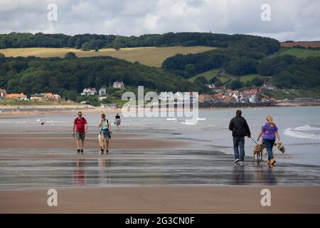 La gente passeggia lungo la spiaggia di Sandsend con la piccola cittadina di pescatori di Sandsend in lontananza nel North Yorkshire. Foto Stock