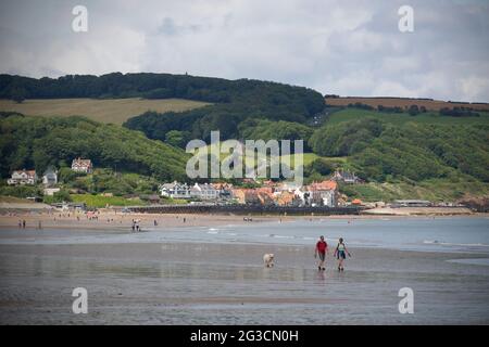 La gente passeggia lungo la spiaggia di Sandsend con la piccola cittadina di pescatori di Sandsend in lontananza nel North Yorkshire. Foto Stock