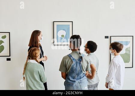 Vista posteriore a diversi gruppi di bambini che indossano maschere in galleria d'arte e guardando dipinti con insegnante femminile Foto Stock