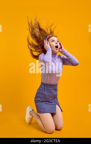 Ritratto di eccitato caucasico Redhead femmina avere capelli volare mentre ascoltano la musica in cuffie, canto canzoni. Bella donna emozionale in casual noi Foto Stock