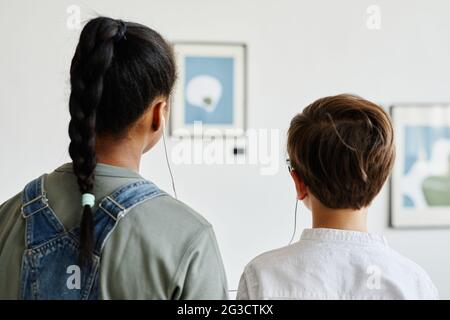 Vista posteriore di due ragazzi adolescenti che guardano i dipinti nella galleria d'arte moderna e indossano le cuffie Foto Stock