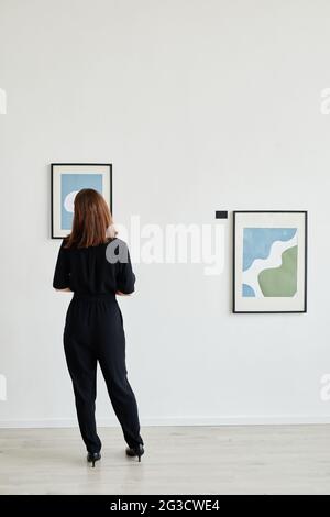 Vista posteriore minima ritratto di giovane donna guardando i dipinti nella galleria d'arte moderna, copia spazio Foto Stock