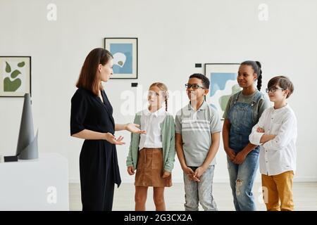 Gruppo variegato di bambini che ascoltano un esperto femminile mentre visitano la galleria d'arte moderna, spazio di copia Foto Stock