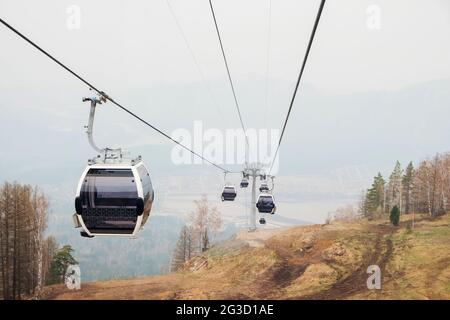 Cabine di ascensore in una stazione sciistica di montagna. Pista di risalita sulla stazione invernale di montagna hilghland in giornata nuvolosa. Funivia per la seggiovia con le persone. Scenico Foto Stock