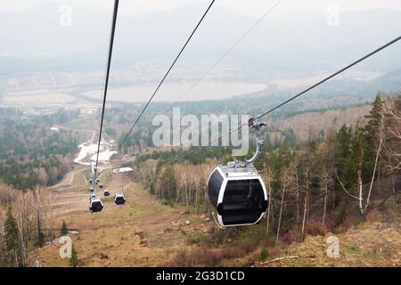 Cabine di ascensore in una stazione sciistica di montagna. Pista di risalita sulla stazione invernale di montagna hilghland in giornata nuvolosa. Funivia per la seggiovia con le persone. Scenico Foto Stock