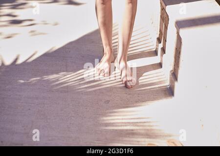 Elegante concetto femminile: Le gambe delle donne nelle tonalità alla moda di un palmo su una parete di pietra naturale beige. Minimo trendy astratto sfondo concreto. Sfondo estivo. Spazio di copia Foto Stock