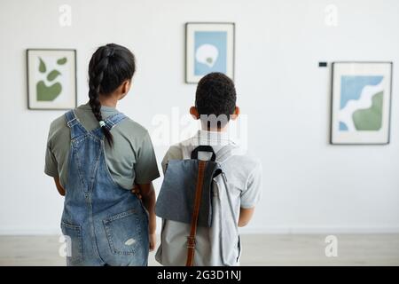 Vista posteriore a due scolari che visitano la galleria d'arte e che guardano i dipinti astratti moderni, spazio di copia Foto Stock