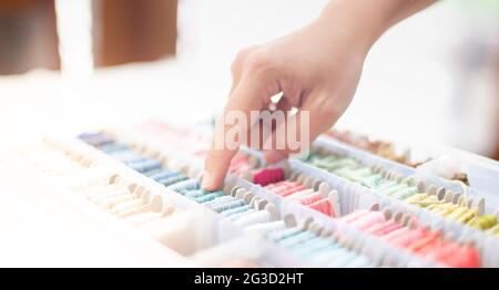 Primo piano le mani di donna su misura che sceglie fili blu oceano e colori diversi nella scatola messo sul tavolo e prepararsi ad utilizzare con cotone bianco e cornice Foto Stock