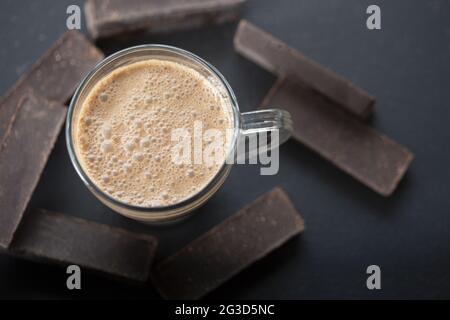 Vista dall'alto del delizioso caffè in un bicchiere e delle barrette di cioccolato fondente su una superficie nera Foto Stock