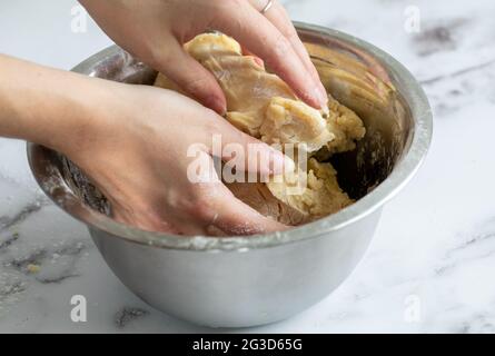 donna miscela a mano gli ingredienti in una ciotola rotonda in metallo su una superficie di marmo bianco con luce naturale Foto Stock