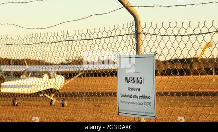 Un primo piano del cartello di avvertimento della Commonwelath of Australia presso un aeroporto regionale o un campo aereo. Nessun segno non autorizzato su una recinzione di sicurezza di filo di pollo e. Foto Stock