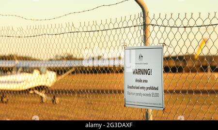 Un primo piano del cartello di avvertimento della Commonwelath of Australia presso un aeroporto regionale o un campo aereo. Nessun segno non autorizzato su una recinzione di sicurezza di filo di pollo e. Foto Stock