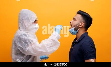 Operatore sanitario in tuta protettiva prendendo tampone orale da un ragazzo potenzialmente infetto. Corona PCR Virus Test con concetto di tampone. Monolocale con sfondo giallo. Foto di alta qualità. Foto Stock