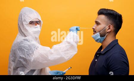 Operatore sanitario in tuta protettiva che prende il tampone nasale da un ragazzo potenzialmente infetto. Corona PCR Virus Test con concetto di tampone. Monolocale con sfondo giallo. Foto di alta qualità. Foto Stock