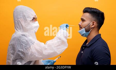 Lavoratore medico in tuta protettiva che prende il tampone nasale da un ragazzo potenzialmente infetto. Corona PCR Virus Test con concetto di tampone. Monolocale con sfondo giallo. Foto di alta qualità. Foto Stock