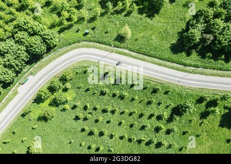 tortuosa pista ciclabile tra alberi e erba verde. vista aerea dall'alto dal drone volante in estate soleggiato giorno. Foto Stock