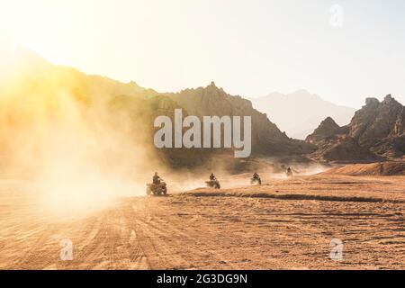 Gruppo di turisti in quad nel deserto egiziano. Un sacco di quad nel giro di polvere sullo sfondo del deserto selvaggio. Tramonto nel deserto oltre il Th Foto Stock