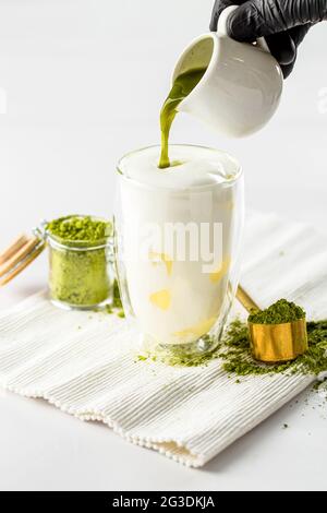 Versare il tè matcha verde in un bicchiere ghiacciato con latte Foto Stock