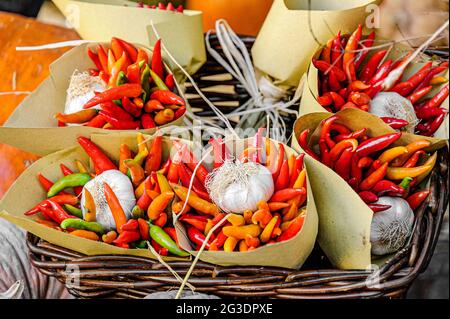 Mazzi di peperoncini colorati con bulbo all'aglio in carta marrone, all'interno di un cesto di rattan. Foto Stock