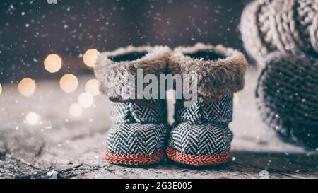 Natale Baby Toy Stivali piccoli e pila pile di felpe a maglia accogliente e tavolo in legno sfondo. Concetto caldo e accogliente. Immagine che tonica la neve Foto Stock