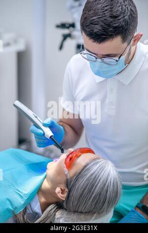 Donna in occhiali protettivi che ha un restauro dentale presso l'ufficio dei dentisti Foto Stock