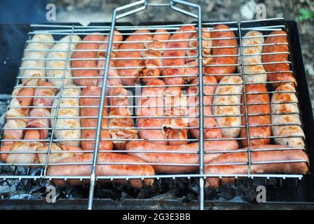 Diversi tipi e colori di salsicce con carne vengono fritti su un fuoco nella foresta Foto Stock