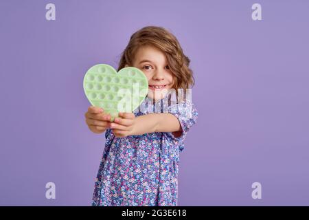 Adolescente ragazza in blu estate fiore stampa vestito tenendo pop it antistress giocattolo su sfondo lavanda, isolare. Foto Stock