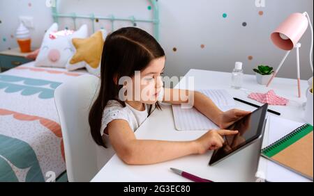 Ragazza che studia a casa con tablet e maschera sul tavolo Foto Stock