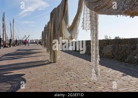 Asciugare le reti da pesca nel porto del villaggio olandese Urk nei Paesi Bassi in una giornata di sole con cielo blu. Foto Stock