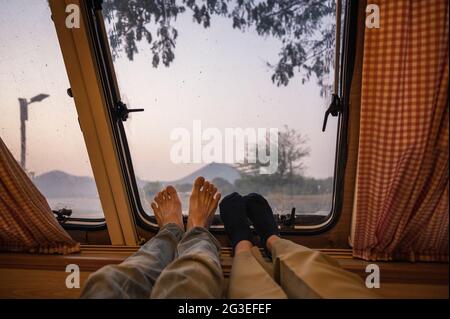 Gambe di giovani coppie che si rilassano in camper con vista sulle montagne sul lago al mattino Foto Stock