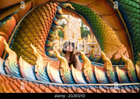 Felice giovane donna asiatica sorridente in colorata statua serpente a Wat Phra che tempio Nong Bua, Ubon Ratchathani Foto Stock