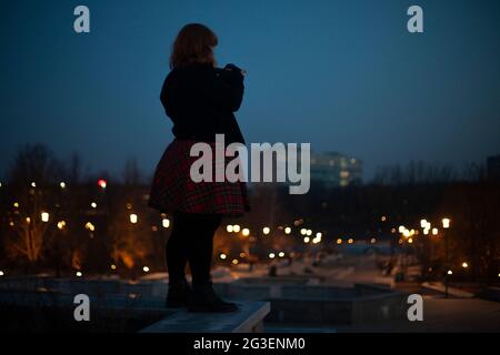 Silhouette Fat girl. La ragazza cammina per la città di notte. La ragazza si erge da sola sullo sfondo della città. Ragazza al buio. Foto Stock