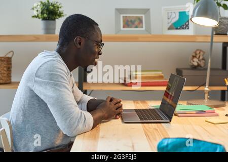 Giovane seduto al tavolo e parlando online con il suo amico sul portatile Foto Stock