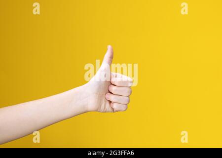 Mano dell'adolescenza con il pollice in su isolato su sfondo giallo. Mostra come, segno positivo. Simbolo, icona di perfetto o Accetta. Foto Stock